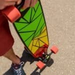 Geel en groen skateboard met geometrisch patroon en rode wielen op asfalt.