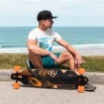 Lange afstand skateboarder op strandpromenade met oceaan op de achtergrond.