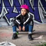 Helmmuts en beschermkleding voor skateboarden, jonge skater zit op skateboard voor graffiti muur.