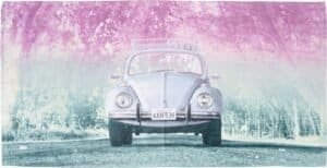Roze en blauwe vintage Volkswagen kever op een weg met bloeiende bomen.
