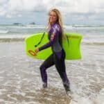 Windsurfster met groen surfboard op het strand onder een bewolkte hemel.