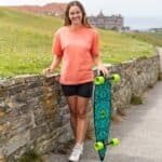 Skateboard en vrouw buiten, skateboarder met langeboard op strandpromenade, lifestyle foto buiten, trendy skate-uitrusting, skatepark en zee in de achtergrond.