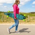 Kleurrijke skateboard met groene wielen, gedragen door vrouw in casual outdoor setting.