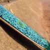 Vrolijk skateboard met blauwe print en groene details op zandondergrond.