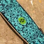 Krijt voor skateboard met blauwe en groene illustraties en kleurrijke details op een zwarte achtergrond.