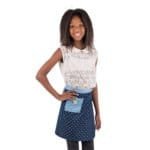 Kleine meisje met lange haar, wit lace top en blauwe rok met hartjes, lachend, staand op witte achtergrond.
