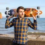 Skateboard met tropisch design, man poseert aan zee, buitenplezier, skateboarden aan het strand.