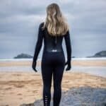 Wetsuit vrouw aan het strand met golven en rotsen op de achtergrond.