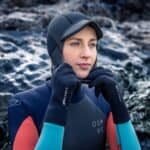 Veiligheidshelm voor watersport en outdooractiviteiten, vrouw op rotskust in wetsuit en handschoenen.