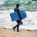Reddingsbrigade in wetsuit met surfplank op het strand.