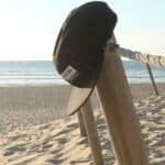 Zwemzwembroek en hoed hangen aan houten paal op het strand.