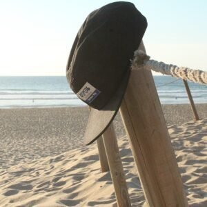 Zwemzwembroek en hoed hangen aan houten paal op het strand.