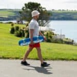 Skateboardenaar met witte hoed en rode shorts wandeling langs de rivier.