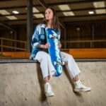 Skateboarder in skatepark met blauwe skateboard, casual outfit en witte sneakers.
