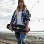 Skateboarder vrouw met skateboard op strand, outdoor skate gear, casual stijl voor buitenplezier.