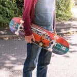 Kleurvolle skateboard met busontwerp, vastgehouden door een persoon in casual kleding buiten.