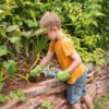 Tuimelende jongen in tuin, gewapend met tuingereedschap, geniet van tuinieren en buitenactiviteiten.