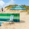Zomerse strandstoel onder een grote blauwe en groene parasol op zandstrand.