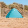 Schattige blauwe campingtent op het strand, omgeven door zand en duinen.