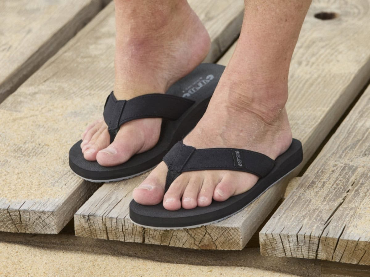 Detail van de comfortabele textiele teenband van de Log slipper aan voet op het strand