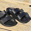 Zwarte Cool Shoe Corp Chill herensandalen op een houten terras bij een strand