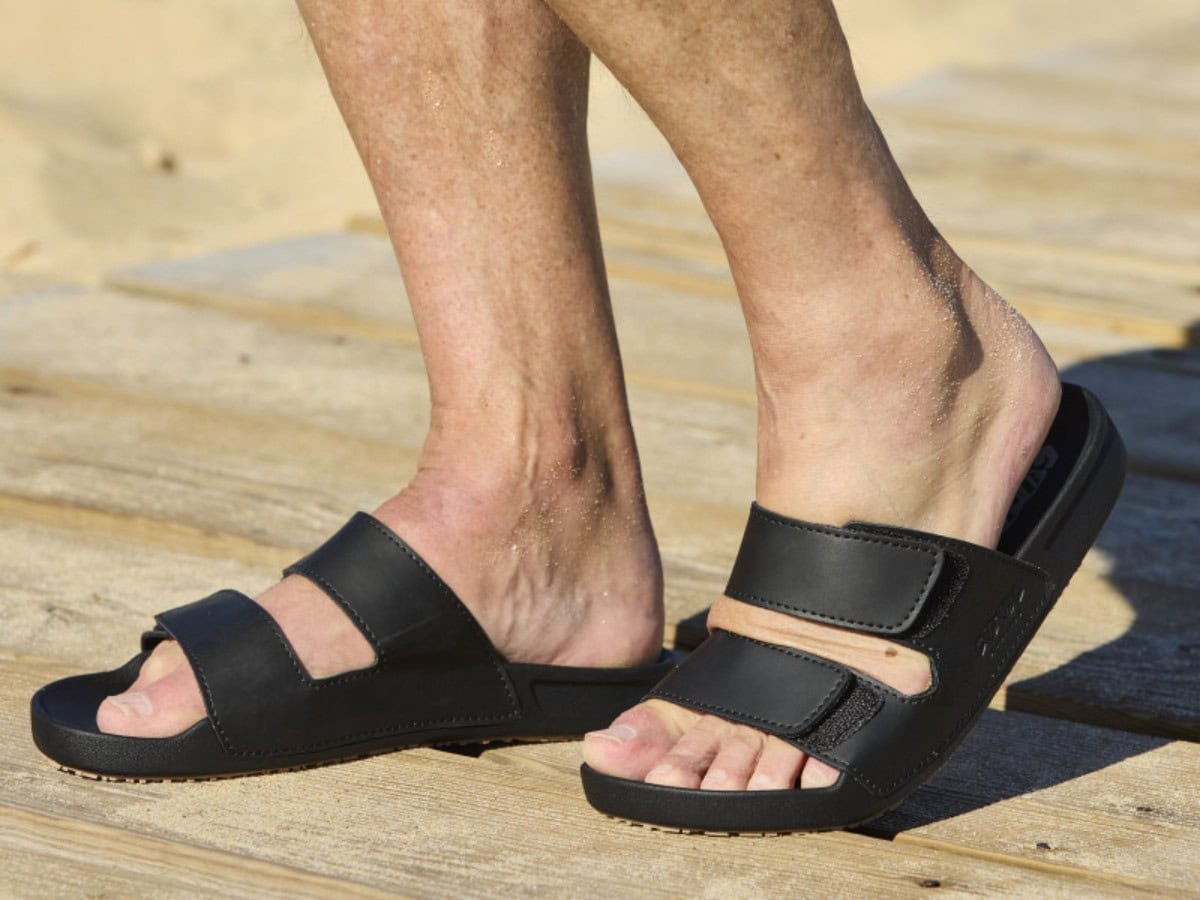 Man draagt zwarte Cool Shoe Corp Chill sandalen terwijl hij bij het strand ontspant