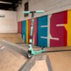 Kleurrijke kick scooter op indoorskatebaan met graffitimuur op achtergrond.