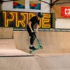 Scooteraar in een binnenbak met vallende rampen en graffiti, draagt een helm en beschermkleding, speelt actief met zijn scooter.